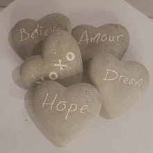Load image into Gallery viewer, These fun and sentimental heart shaped stones are perfect for expressing ones feelings of love, hope, dream and belief. Comes in an assorted set of 5. Give all 5 to that special someone, or spread the love and give one to all your special someones. Don't forget to keep one as a reminder to yourself. Each Set Includes 5 Stones*: Believe Hope Dream Amour XOXO Materials: Cement Dimensions: 2.7"L x 2.5"W (each stone) Fragile in nature; handle with care *Must be purchased as a set of 5 assorted stones.