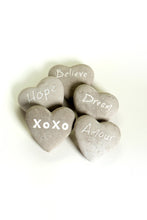 Load image into Gallery viewer, These fun and sentimental heart shaped stones are perfect for expressing ones feelings of love, hope, dream and belief.  Comes in an assorted set of 5.  Give all 5 to that special someone, or spread the love and give one to all your special someones.  Don't forget to keep one as a reminder to yourself.   Each Set Includes 5 Stones*:  Believe Hope Dream Amour XOXO Materials: Cement   Dimensions: 2.7"L x 2.5"W (each stone)  Fragile in nature; handle with care  *Must be purchased as a set of 5 assorted stones.