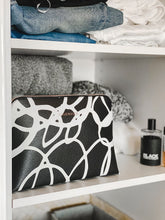 Load image into Gallery viewer, The Bardot Swirl Case is a funky, black and white art print case with a firm structure so it stands tall in your bathroom.  Perfect as a make-up or toiletry case for those weekend getaways.  It's Rose Gold zippr is a beautiful additional detail.  Pair it with the Emma Hanging Toiletry case for an Exclusive Bundle!  Internal Features:  2 Flat Pockets Lining: Polyester Sateen Twill Secure Zip Material: Vegan Leather  Hardware: Rose Gold  Dimensions: H18.5 x W26 x D9 cm. Shown: Bardot Case on Shelf