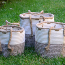 Load image into Gallery viewer, Add these beautiful storage baskets to your living space.  These two-tone cotton rope baskets are designed in natural shades of beige and brown. Jute rope handles at the sides make it easy to move the baskets around any room.   3 sizes to choose from:  Small:  8" Diameter Medium:  9.5" Diameter Large:  10.5" Diameter Get creative and use them as the base for an amazing gift basket filled with our great products.  Material:  Cotton, Jute.