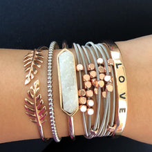 Load image into Gallery viewer, The Love Metal Cuff Bracelet in Rose Gold features a simplistic bangle with the word LOVE inscribed on the outside. Wear this bangle on its own to make a simple statement or as part of the Lainey Stack to make the perfect stack. Exclusively from Kinsley Armelle.   Details:  Style: Cuff Material: 18K Rose Gold Ion Plated Stainless Steel Size: 6.5 - 8 Inch Circumference. Shown:  Lainey Stack