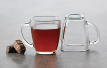 Load image into Gallery viewer, Enjoy the contemporary style, and seeing what's inside, when you sip from this square clear glass mug.  Serve up hot toddies, cappuccinos, lattes, tea, hot cocoa, and more. Constructed from high-quality glass for everyday durability.  Pair it with our beautiful teas and accessories for the ultimate tea set gift-box.  Size:  4" L  Material:  Clear Glass  Capacity:  14oz