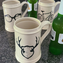 Load image into Gallery viewer, Add to your drinkware collection with these unique beige ceramic beer steins.  Perfect for entertaining on the patio or cottage deck, or chilling in front of the tv.  Pair them with your favourite bottle for a great Father's Day, Birthday or Just Because gift.  3 styles to choose from:  Antlers Sunglasses Bicycle Capacity:  18oz  Material:  Ceramic