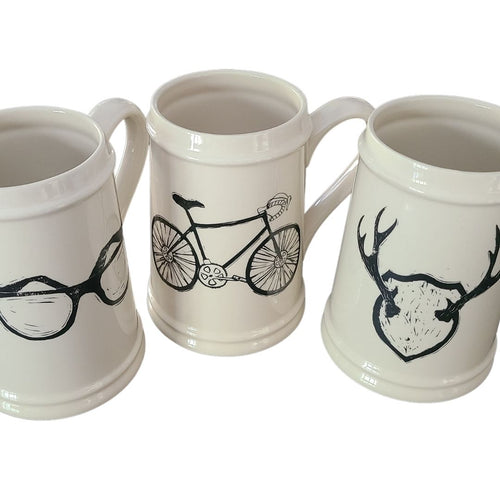 Add to your drinkware collection with these unique beige ceramic beer steins.  Perfect for entertaining on the patio or cottage deck, or chilling in front of the tv.  Pair them with your favourite bottle for a great Father's Day, Birthday or Just Because gift.  3 styles to choose from:  Antlers Sunglasses Bicycle Capacity:  18oz  Material:  Ceramic
