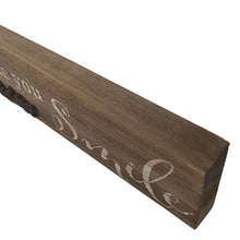 Load image into Gallery viewer, This farmhouse style painted wood plaque with printed "Enjoy the Moments That Make You Smile" sentiment is the perfect adornment for any home, with an added decorative iron motif.  Hang it or set it on any surface in your foyer, kitchen, familyroom or hallway so everyone can see it.    Makes a great hostess, mother's day or just because gift too.  Size: 16" x 2.5" x.75  Material: Pine wood/Iron