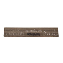 Load image into Gallery viewer, This farmhouse style painted wood plaque with printed "Enjoy the Moments That Make You Smile" sentiment is the perfect adornment for any home, with an added decorative iron motif.  Hang it or set it on any surface in your foyer, kitchen, familyroom or hallway so everyone can see it.    Makes a great hostess, mother's day or just because gift too.  Size: 16" x 2.5" x.75  Material: Pine wood/Iron