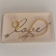 Load image into Gallery viewer, Our &quot;Love&quot; Trinket Dish features a pretty retro pink plate with the word &quot;love&quot; printed in shimmering gold. Perfect for storing your favourite jewellery and trinkets, and perfect as a daily reminder to you or that someone special to love yourself. Size: 6.5&quot; x 4&quot; Material: Ceramic *Hand wash only. Shown: with jewelery
