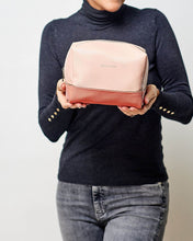 Load image into Gallery viewer, The Tara Cosmetic case is a beautiful top-zipper makeup bag perfect for travel or storage. Gorgeous two-tone pink colours and a soft texture, this travel case is spacious enough to fit all your makeup and toiletries for a weekend away. Features: Lining: Polyester Sateen Twill Closure: Secure Zip Material: Vegan Leather Hardware: Light Gold Dimensions: W23 x H11 x D11cm.  Shown: Person holding Tara Pink Cosmetic Case
