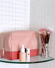 Load image into Gallery viewer, The Tara Cosmetic case is a beautiful top-zipper makeup bag perfect for travel or storage. Gorgeous two-tone pink colours and a soft texture, this travel case is spacious enough to fit all your makeup and toiletries for a weekend away. Features: Lining: Polyester Sateen Twill Closure: Secure Zip Material: Vegan Leather Hardware: Light Gold Dimensions: W23 x H11 x D11cm. Shown: Tara Pink Cosmetic Case on shelf
