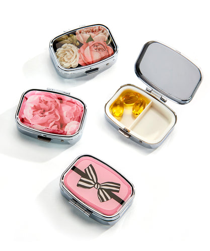 Keep your pills organized in this practical, pretty and stylish pill box that features two compartments inside and a beautiful design on the lid.  Perfect for your pocket, purse and gym bag.  3 Styles to choose from:  Multi-Roses Pink Rose Black Bow