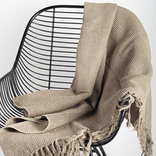 Load image into Gallery viewer, This beautiful Throw Blanket has a classic waffle weave pattern adorned with whimsical fringes.  Light, yet cozy.  Matches perfect with any decor.  Size:  68 × 52 in  Colour:  Taupe  Material:  Cotton. Shown:  Blanket thrown over a chair.

