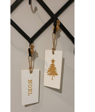Load image into Gallery viewer, These fun and whymsical Christmas Hangers will create the perfect welcome this holiday season. With a Christmas Message on one side, and a Winter Symbol on the other, this white and gold decor will look beautiful in any room. Put it anywhere...doorknobs, walls, mantles...and you can even use it as ornaments on your tree. 2 Styles to choose from: Cheer Noel. Size: 7.5 x 3.5 x .25&quot;. Shown: Noel/Christmas Tree
