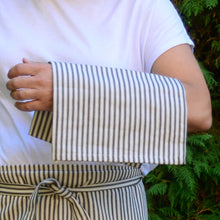 Load image into Gallery viewer, This classic Ticking Stripe patterned, 100% cotton tea towel will compliment any kitchen design. Machine wash gentle cycle. Measures: ﻿18&quot; w x 28&quot; Shown: Person holding towel
