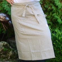 Load image into Gallery viewer, Look professional in this stylish and classic Ticking Stripe patterned, 100% cotton apron! Comes complete with a utility front pocket. Machine wash gentle cycle. Measures: ﻿34&quot; w x 34&quot; l  Shown: Person wearing Ticking Stripe Apron
