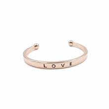 Load image into Gallery viewer, The Love Metal Cuff Bracelet in Rose Gold features a simplistic bangle with the word LOVE inscribed on the outside. Wear this bangle on its own to make a simple statement or as part of the Lainey Stack to make the perfect stack. Exclusively from Kinsley Armelle.   Details:  Style: Cuff Material: 18K Rose Gold Ion Plated Stainless Steel Size: 6.5 - 8 Inch Circumference
