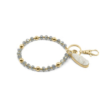 Load image into Gallery viewer, This Beaded Bracelet Keychain features a glimmering druzy white stone that will truly enchant those around you with its unique texture. The keychain has a 18k gold ion-plated stainless steel teardrop setting. It is surrounded with gold metal and grey glass beads for an elegant look.  Exclusively from Kinsley Armelle.   Details:  Materials: 18K Yellow Gold Ion Plated Stainless Steel, druzy stone, glass and metal beads Size: 3&quot; d Key Ring
