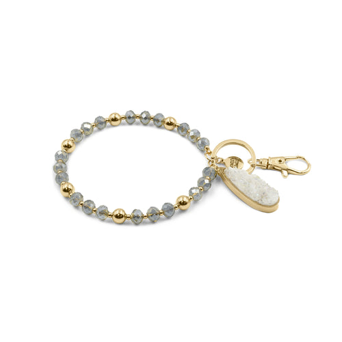 This Beaded Bracelet Keychain features a glimmering druzy white stone that will truly enchant those around you with its unique texture. The keychain has a 18k gold ion-plated stainless steel teardrop setting. It is surrounded with gold metal and grey glass beads for an elegant look.  Exclusively from Kinsley Armelle.   Details:  Materials: 18K Yellow Gold Ion Plated Stainless Steel, druzy stone, glass and metal beads Size: 3