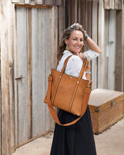 Load image into Gallery viewer, The Nutmeg Nevada Bag is a great tote style which can double as a laptop or work bag. Featuring a luxurious suedette lining, this shoulder bag is spacious and functional with enough room to carry all your essentials and more! Features: 2 Slip Pockets 1 Zip Pocket Feet on Base Internal Lining: Suedette Strap: Height 25cm Extension Strap: Detachable Webbing 41cm Magnetic Clasp Material: Vegan Leather Hardware: Light Gold Dimensions: H31 x W41 x D11 cm. Shown: Person holding bag over shoulder
