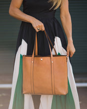 Load image into Gallery viewer, The Nutmeg Nevada Bag is a great tote style which can double as a laptop or work bag. Featuring a luxurious suedette lining, this shoulder bag is spacious and functional with enough room to carry all your essentials and more! Features: 2 Slip Pockets 1 Zip Pocket Feet on Base Internal Lining: Suedette Strap: Height 25cm Extension Strap: Detachable Webbing 41cm Magnetic Clasp Material: Vegan Leather Hardware: Light Gold Dimensions: H31 x W41 x D11 cm. Shown: Person holding bag as a tote

