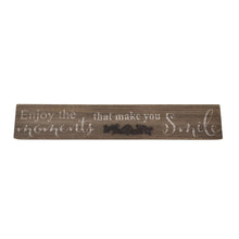 Load image into Gallery viewer, This farmhouse style painted wood plaque with printed &quot;Enjoy the Moments That Make You Smile&quot; sentiment is the perfect adornment for any home, with an added decorative iron motif.  Hang it or set it on any surface in your foyer, kitchen, familyroom or hallway so everyone can see it.    Makes a great hostess, mother&#39;s day or just because gift too.  Size: 16&quot; x 2.5&quot; x.75  Material: Pine wood/Iron
